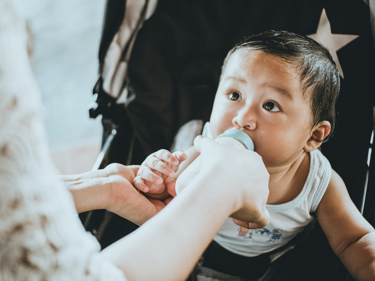 A baby sitting upright while a parent holds the bottle