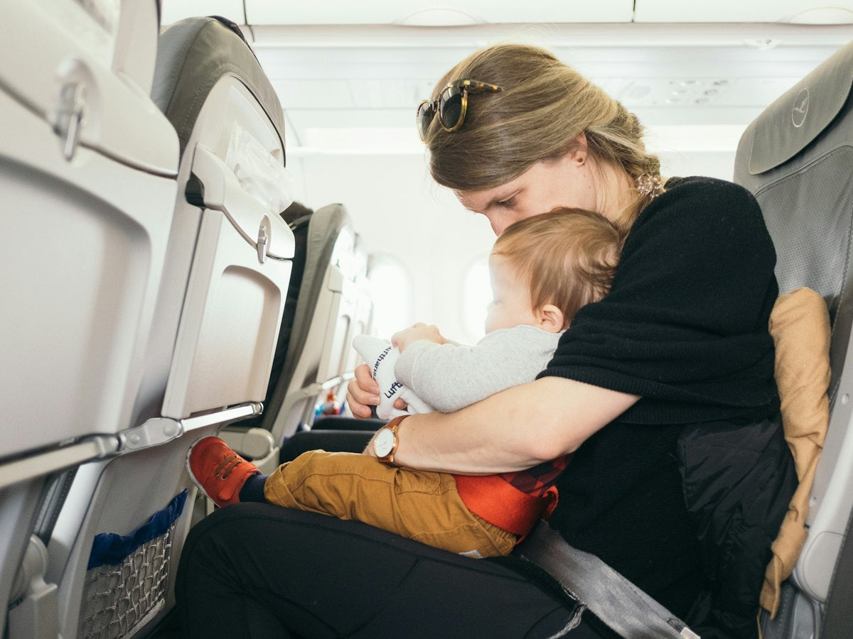 A parent holding a baby in an airplane seat by the window