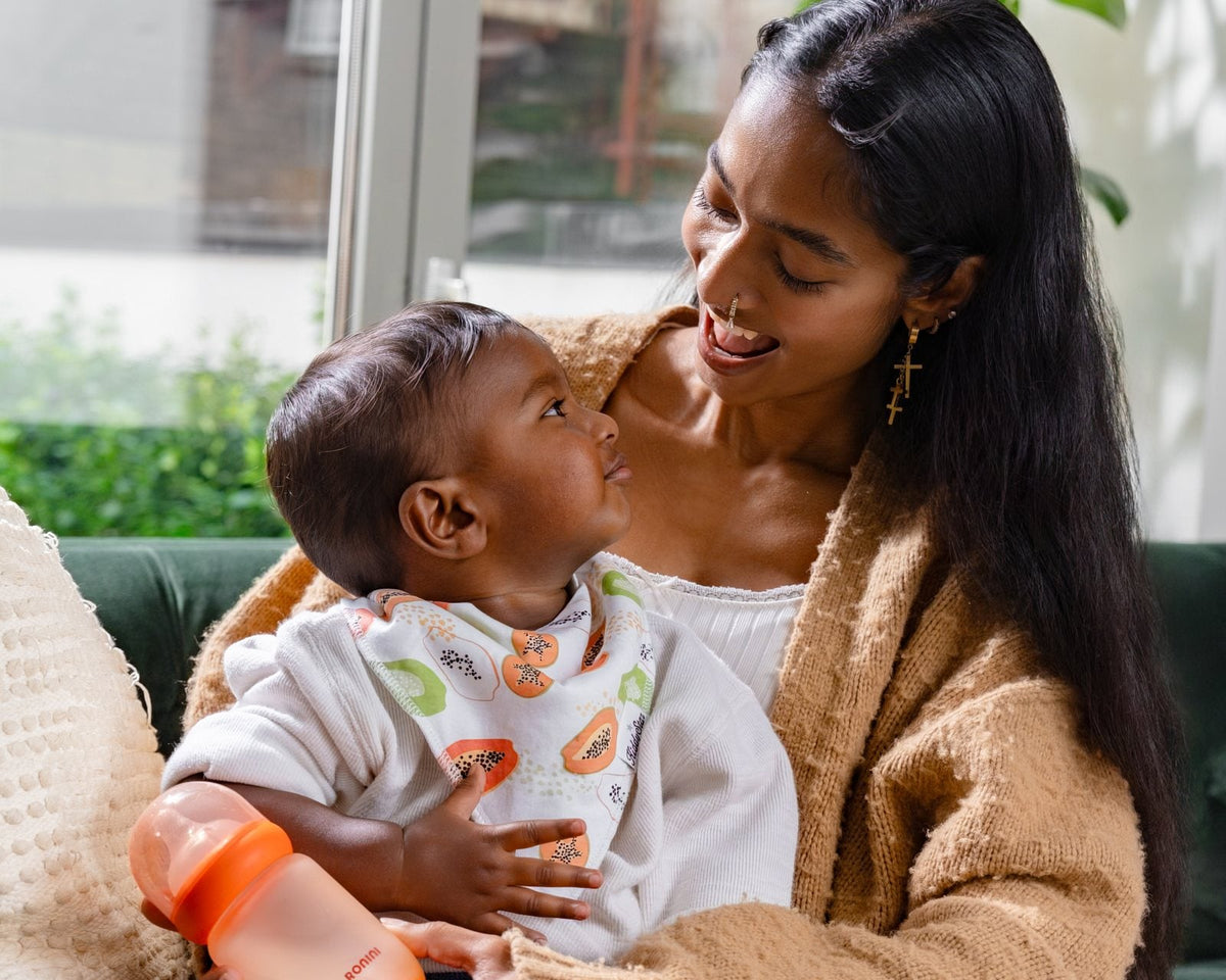 A parent smiling at their baby, a Ronini bottle in the baby’s hands