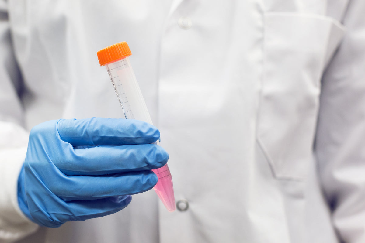 A gloved hand holding a test tube with an orange cap