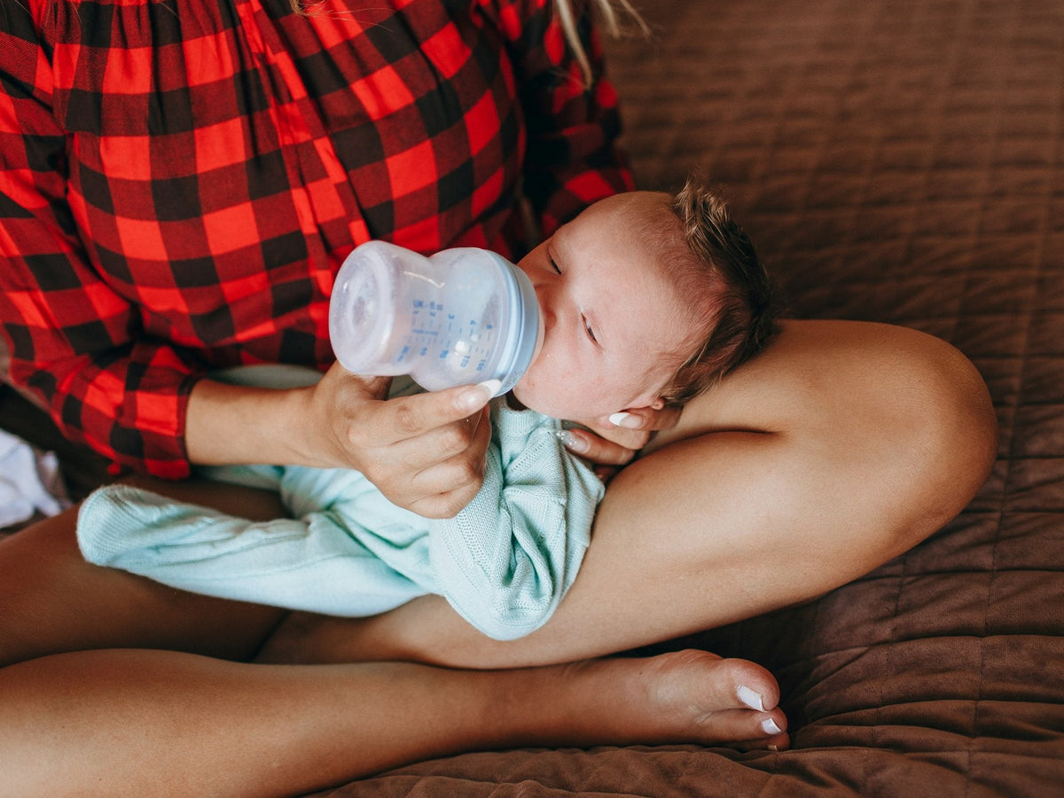 A parent feeding a newborn a bottle on their lap