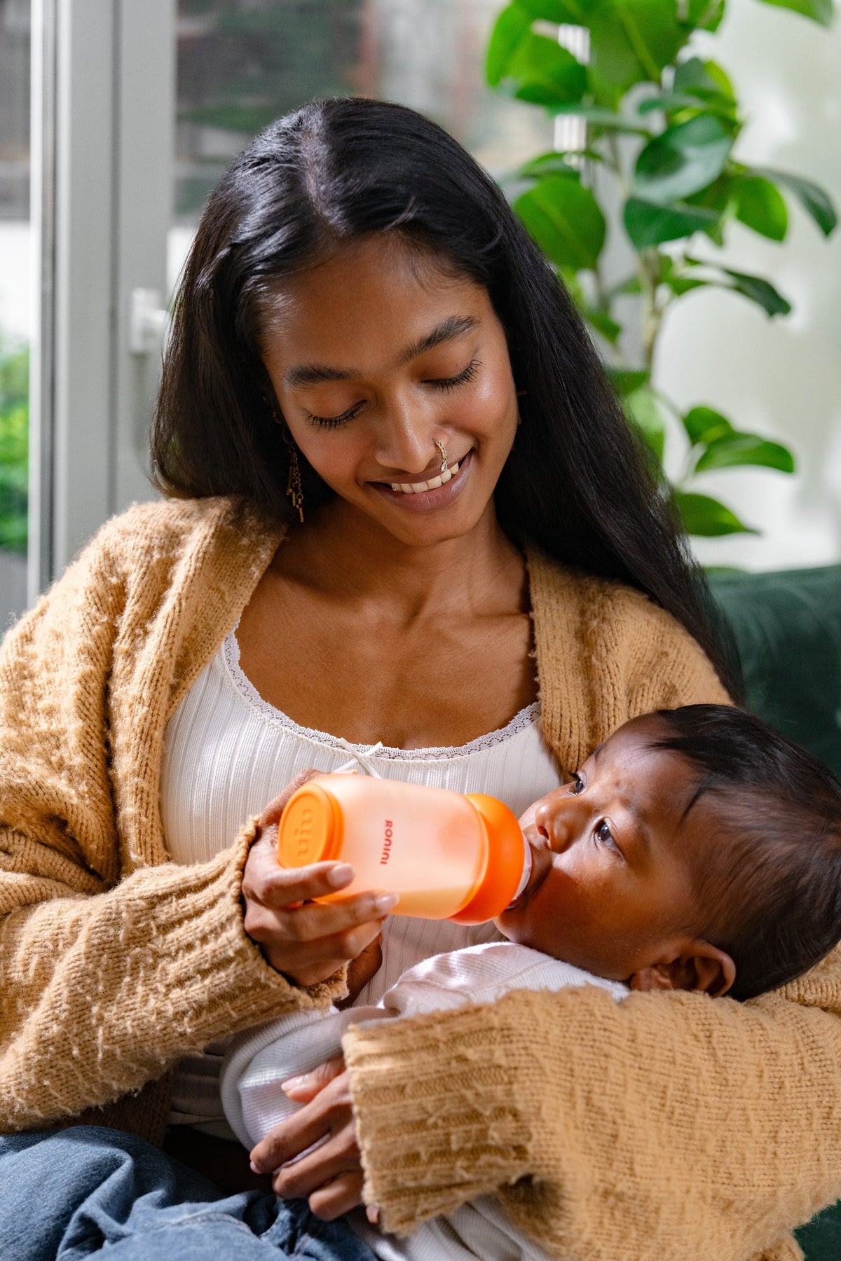 A parent feeding a baby with The Wrapped Glass Bottle by a window