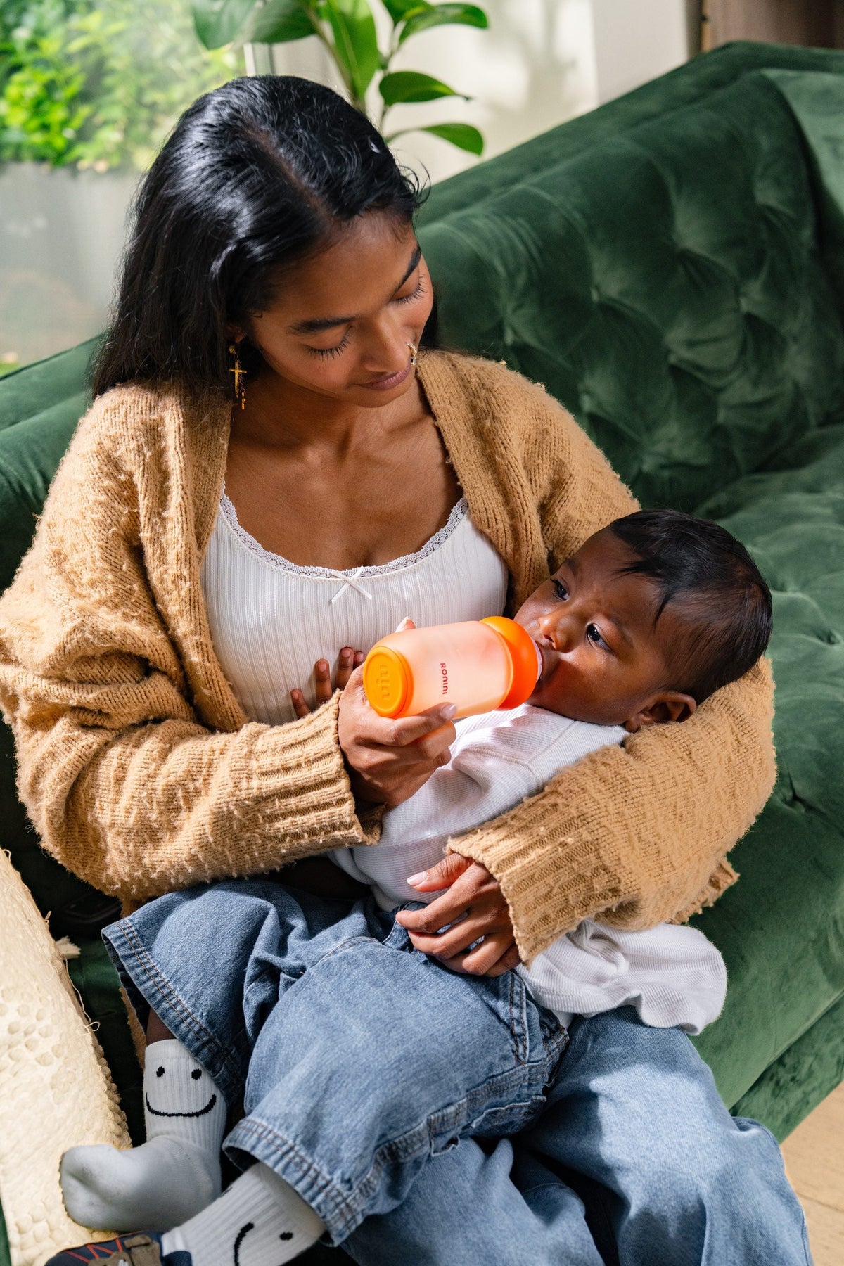 A parent feeding a baby with The Wrapped Glass Bottle on a green sofa