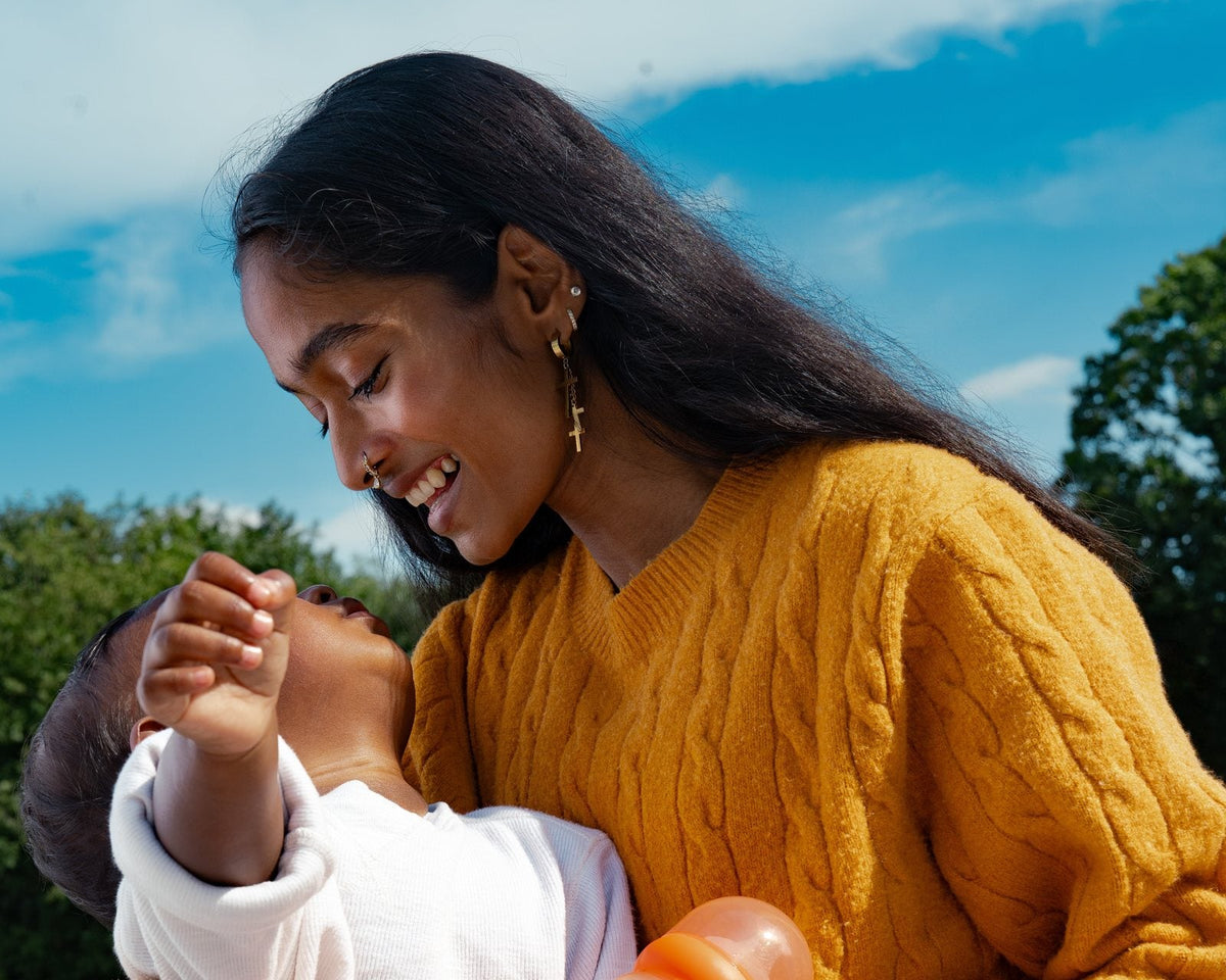 A parent holding their baby up outdoors, laughing