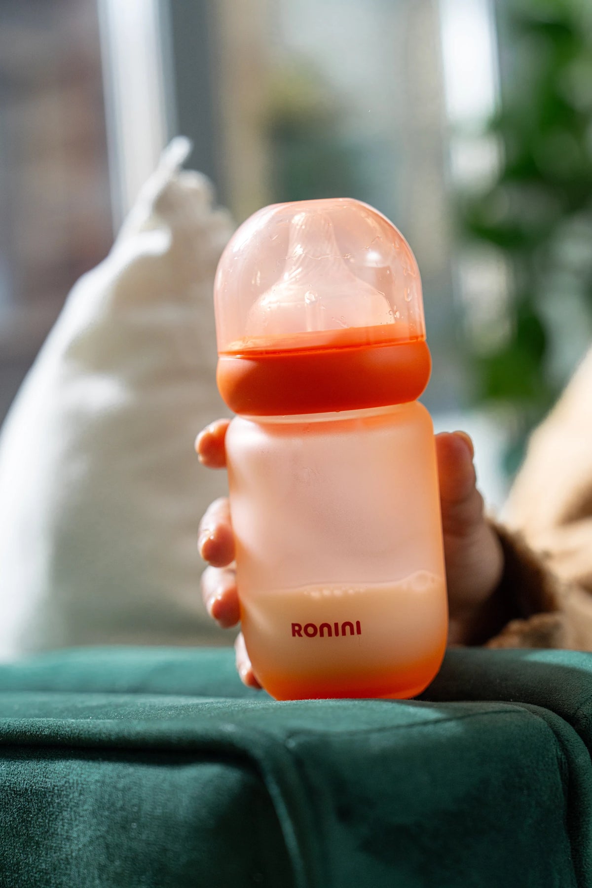 A hand holding a 5 oz Wrapped Glass Bottle on the sofa