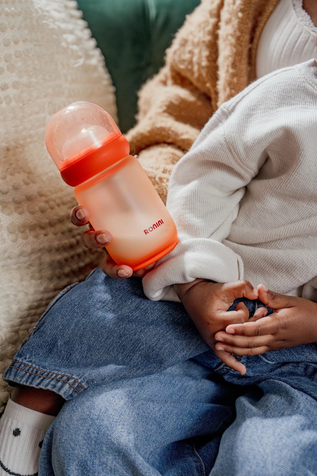 A hand holding The Wrapped Glass Bottle on the sofa