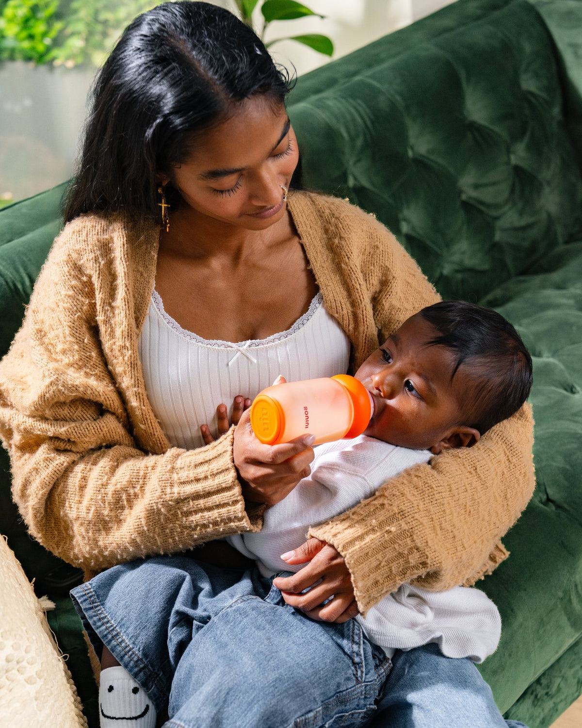 A parent feeding a baby with The Wrapped Glass Bottle on a green sofa
